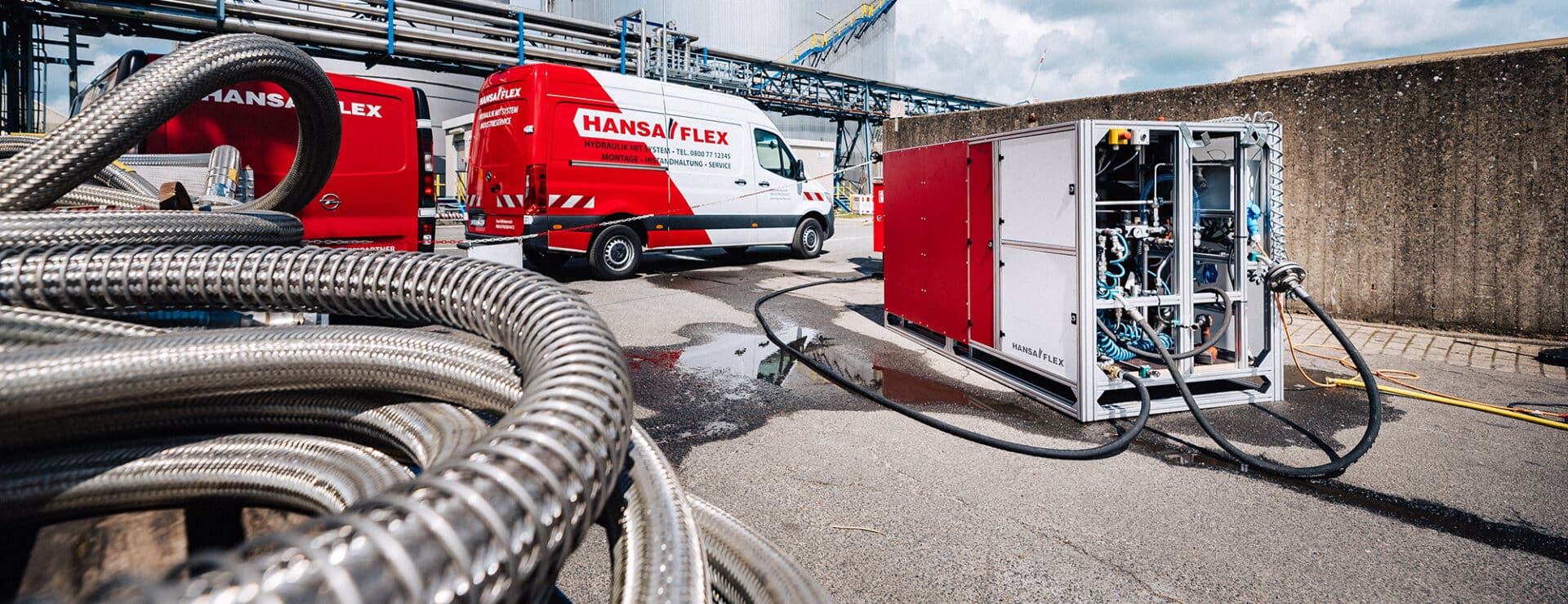 Industrieschlauchprüfung von HANSA-FLEX mit Industrieschläuchen im Vordergrund und Autos von HANSA-FLEX für die Prüfung im Hintergrund